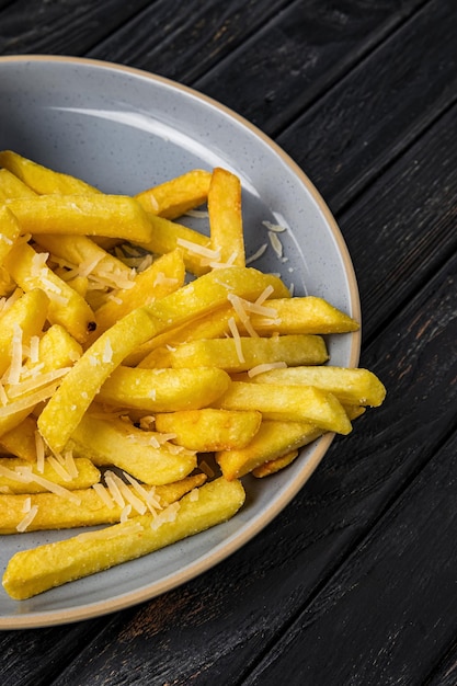 Closeup of french fries with cheese on a plate on dark wooden backdrop