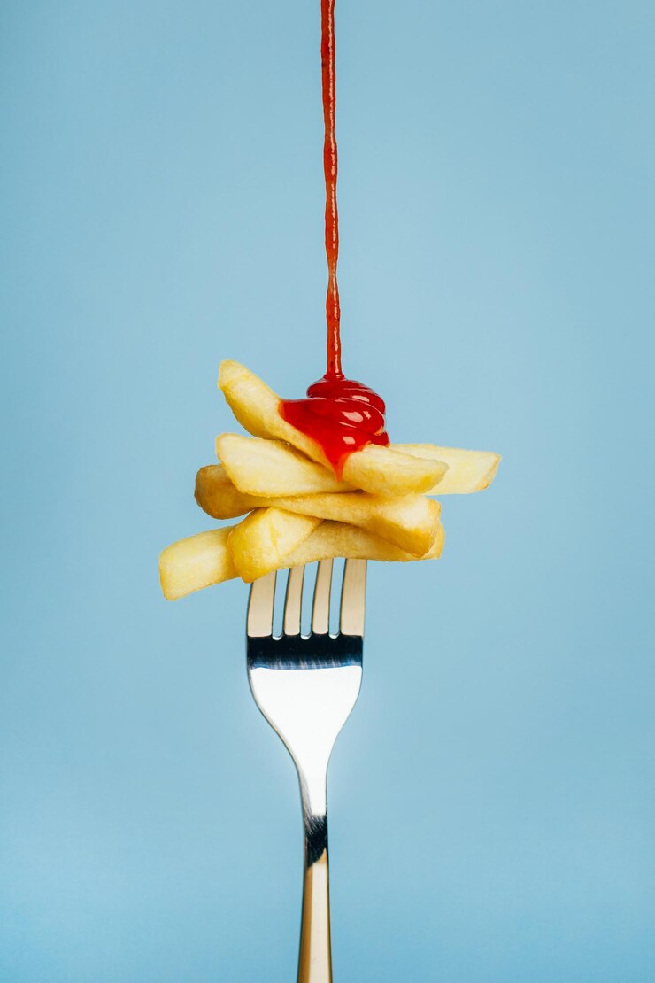 Closeup on french fries with pouring ketchup on a fork on a blue background