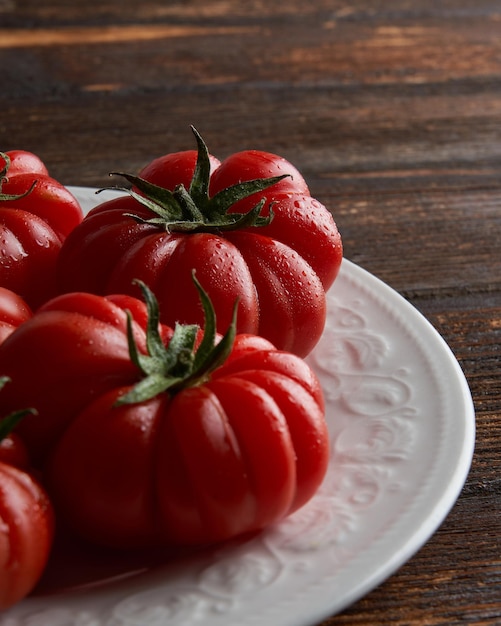 Closeup of Fresh red tomatoes raf on white plate on wooden background Food concept