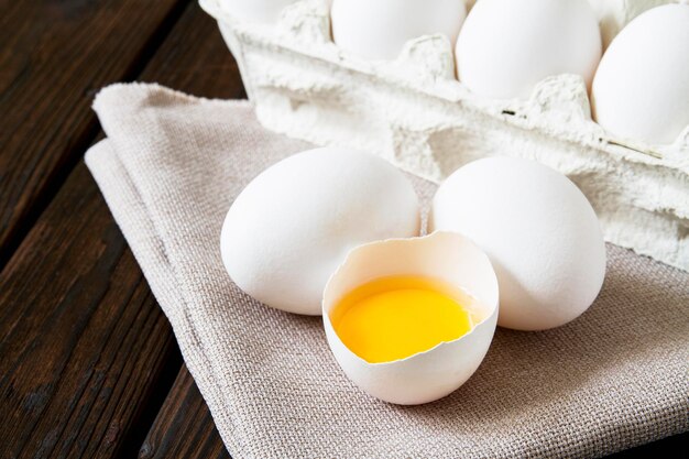 Primo piano di uova di gallina bianche fresche e tuorlo d'uovo su tessuto di lino e fondo di legno scuro