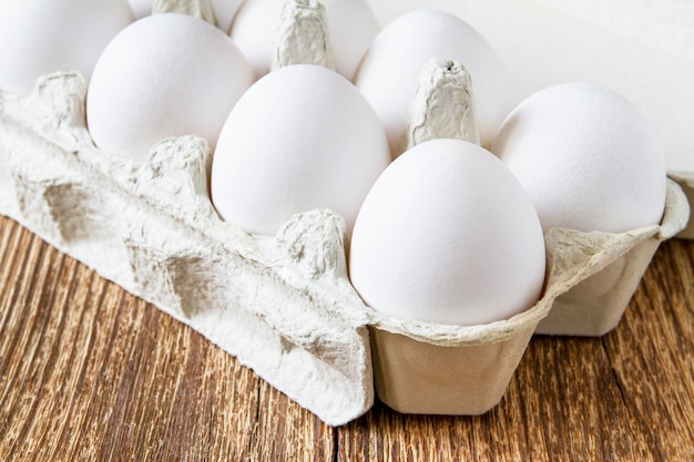 Closeup of fresh white organic chicken eggs in the paper tray on wooden background