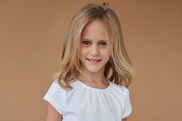 Closeup front portrait of cheerful little girl with wavy blond hair, dressed in white clothes