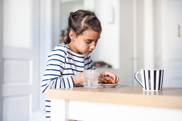 Closeup front view of a elementary school girl eating a burger at a home