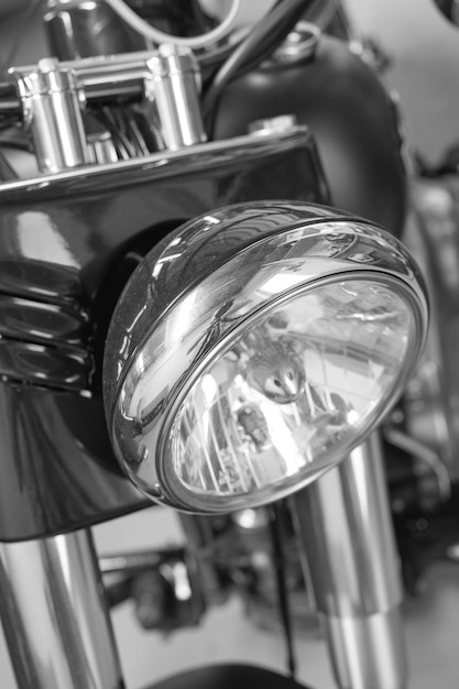 Closeup front view of a head light on a motorbike a monochrome\
vintage motorcycle in black and white one modern silver chrome\
transportation vehicle maintenance on a classic retro custom\
bike