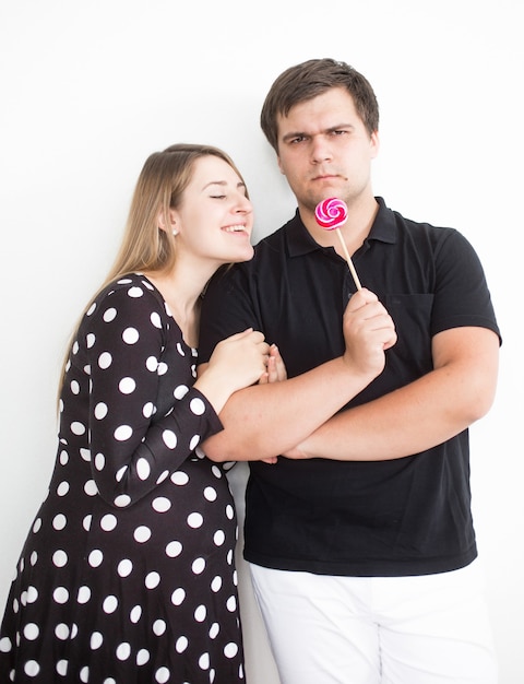 Closeup funny portrait of young man holding lollipop and giving in to girlfriend