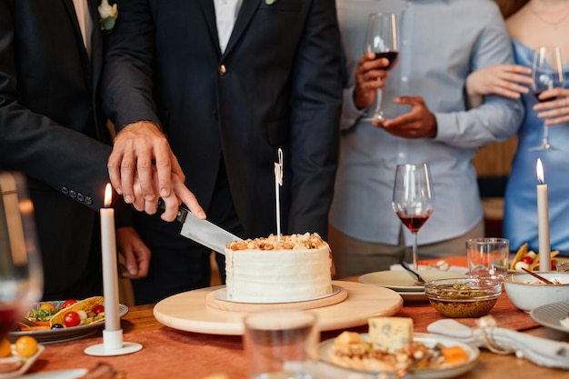 Primo piano della torta di taglio delle coppie gay insieme durante lo spazio della copia del matrimonio dello stesso sesso del ricevimento di nozze