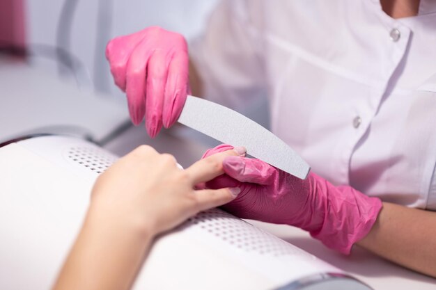 Closeup of a girl doing a manicure in a beauty salon Nail care A manicurist in pink gloves files a client39s nails Cosmetic procedures