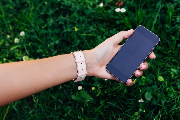 closeup of a girl hand that holds the phone in the background of green grass