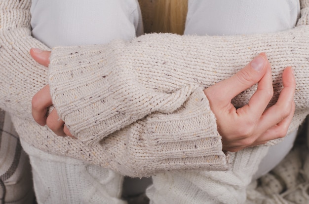 Closeup of girl's hands in casual wool sweater hugging her knees to her chest, feeling lonely