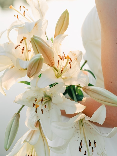 Closeup of a girl in a white dress holding a bouquet of white lilies. against the lake