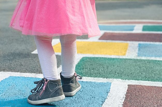 Closeup of girls legs in a pink dress and hopscotch drawn on asphalt outdoor activities