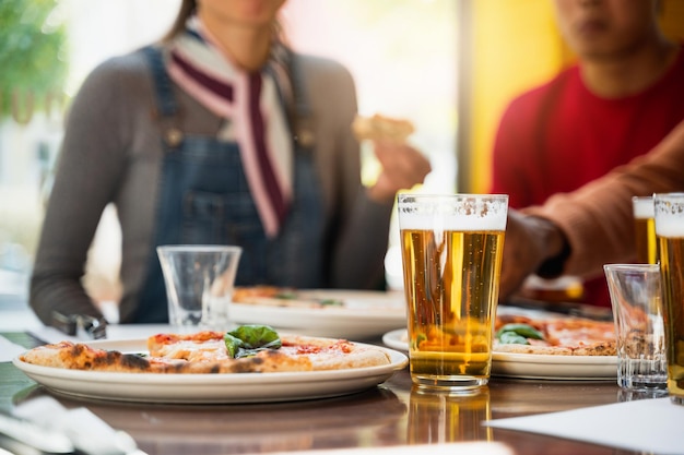 Closeup glass of beer with froth on table next to a plate with Margherita pizza