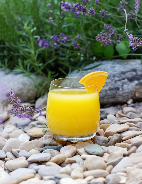夏の庭で熟したオレンジのスライスを添えた新鮮なオレンジ ジュースのガラスのクローズ アップ