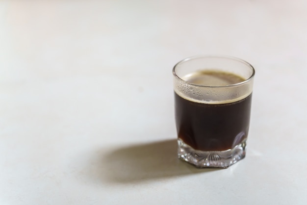 Closeup of glass of hot black coffee Americano with sunlingt and shadow on white table