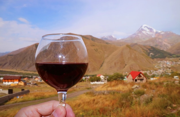 Primo piano un bicchiere di vino rosso in mano d'uomo contro le catene montuose