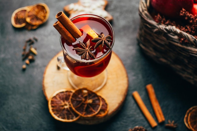 Foto close-up di un bicchiere di vino caldo cannella e cardamomo su uno sfondo nero con gli ingredienti per la bevanda