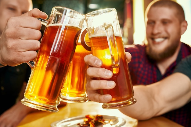 Closeup of glasses of beer in hands of happy company in pub