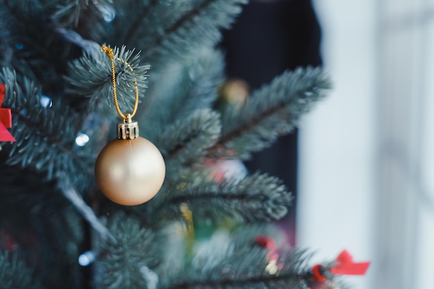 Closeup of gold ball hanging from a decorated Christmas tree with copy space. Christmas and New year holidays background.