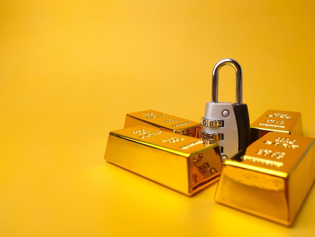 Closeup of gold bars bullions and a padlock isolated on a yellow background - finance concept