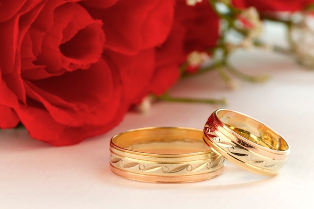 Closeup of gold rings for a romantic wedding with red flowers