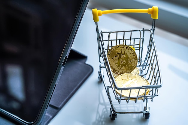 Closeup of Golden bitcoins or cryptocurrency coin or symbols in shopping cart and tablet in white table Future currency concept