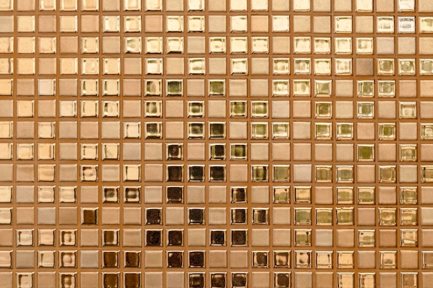 Closeup of goldencolored square glass tiles covering the bathroom wall texture as a background