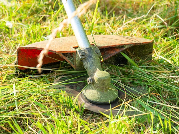 Foto primo piano di un tagliaerba con un ugello a forma di coltello di metallo cura della trama che taglia l'erba erba alta erbacce vista dal basso da terra