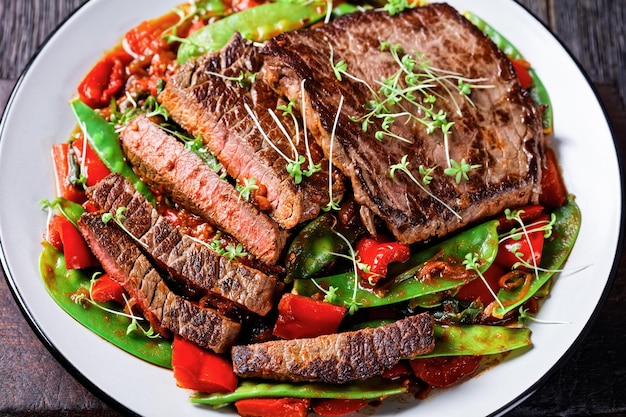 Closeup of grilled Beef Flank Steak served with ragout of braised in tomato sauce veggies and herbs red pepper mangetout and  thyme