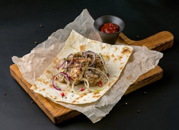 Closeup of grilled chicken meat with pita bread and pickled onions on a dark background Meat on a wooden board