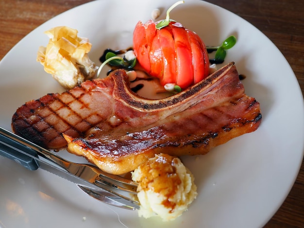 Closeup grilled pork chop steak decorated with sliced tomato on white dish