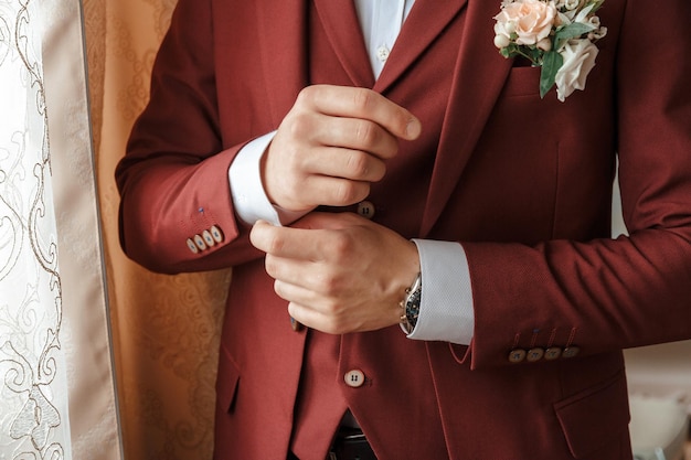 Closeup of a groom in maroon suit correcting a sleeve