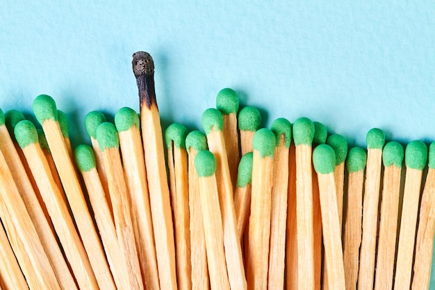 Closeup of a group of matches with green heads and with one burnt match on a blue background