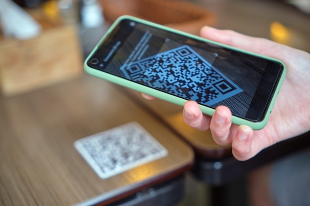 Foto primo piano della mano dell'ospite che ordina il pasto al ristorante durante la scansione del codice qr con il telefono cellulare per il menu online.