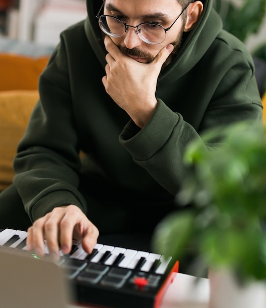 自宅のラップトップ コンピューターでポータブル MIDI キーボードを使用して電子音楽トラックを録音するクローズ アップの男