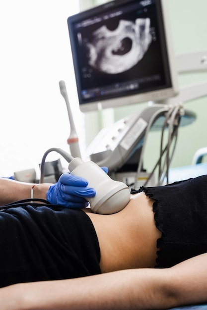 Foto il ginecologo del primo piano esegue l'ecografia per la giovane donna incinta all'inizio del periodo di gravidanza e guarda sullo schermo in ospedale gravidanza e maternità