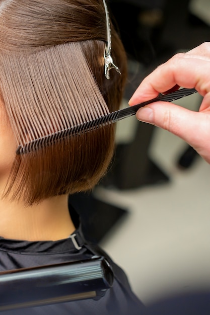 Closeup of a hairdresser straightening short brown hair with hair iron in a hair salon