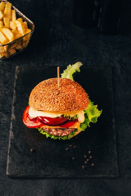 Photo closeup of a hamburger on a black table with fries in the background