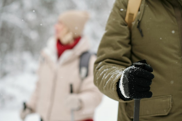 Closeup of hand of active man holding trekking stick while strolling in forest