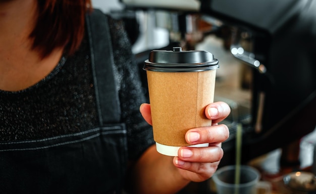 Foto primo piano della mano il barista tiene in mano il caffè caldo in una tazza di carta da asporto caffè da asporto