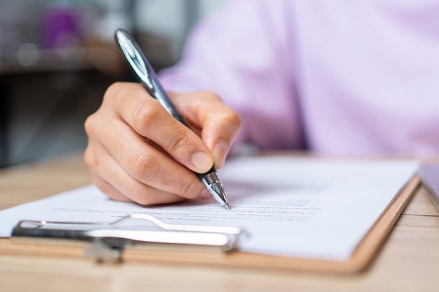 closeup hand of businesswoman writing signing documents on paper in office desk