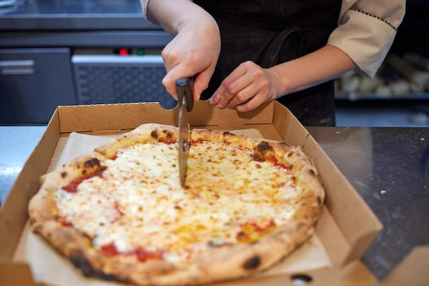 Closeup hand of chef baker in white uniform cutting pizza at kitchen.