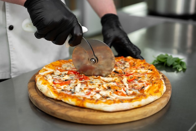 Closeup hand of chef cuts freshly prepared pizza slices at kitchen