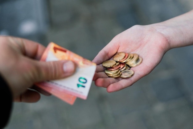 Closeup of a hand giving coins to another hand with banknotes