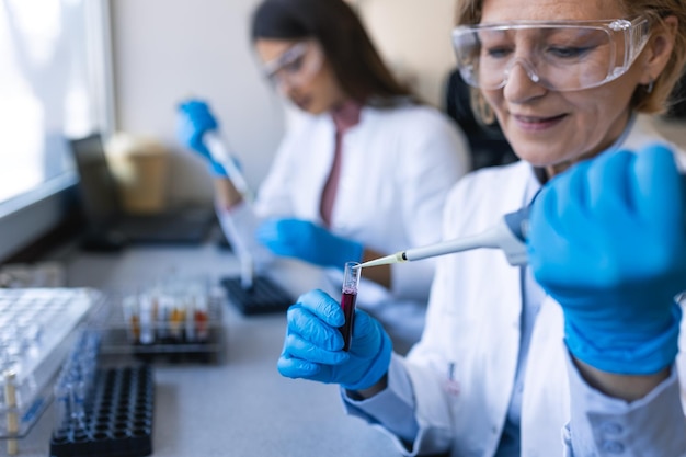 유전학 연구를 위한 현대 의료 장비를 갖춘 혁신적인 제약 실험실에서 테스트 튜브로 작업하는 동안 마이크로 피펫을 사용하여 장갑에 손을 닫습니다.