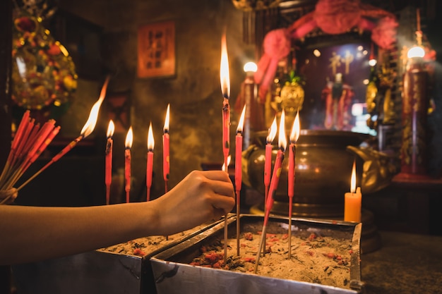 Photo closeup of the hand hold the red candles in the old incense pot.