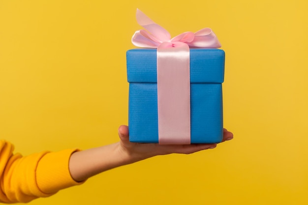 Closeup hand holding blue gift box with pink ribbon decoration romantic surprise for Valentine39s day nice Christmas holiday present birthday celebration studio shot isolated on yellow background