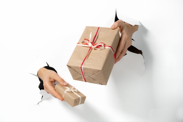 Closeup hand holding gift with ribbon through a torn paper