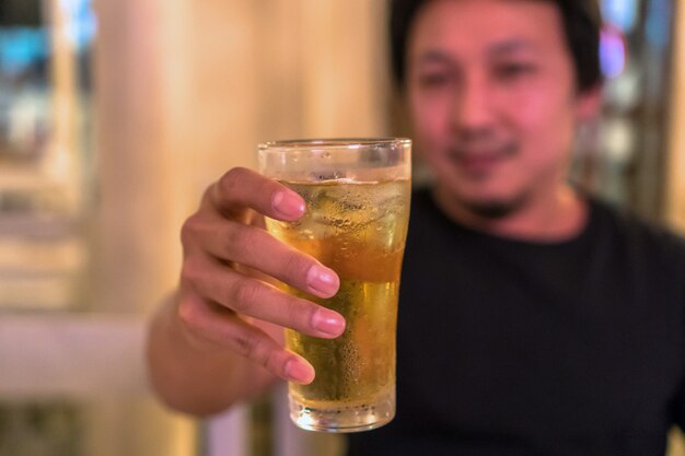 Photo closeup hand holding glass of beer from asian young man in happiness action in pub and res