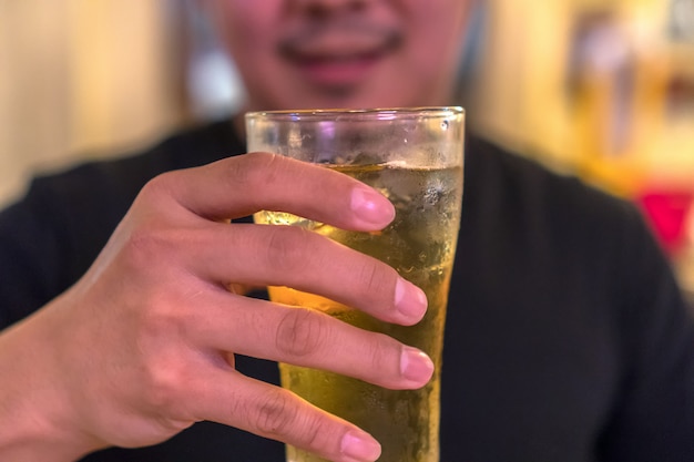 Closeup hand holding glass of beer from Asian young man in happiness action in pub 