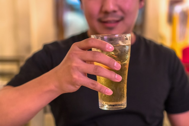 Mano del primo piano che tiene vetro di birra dal giovane asiatico nell'azione di felicità